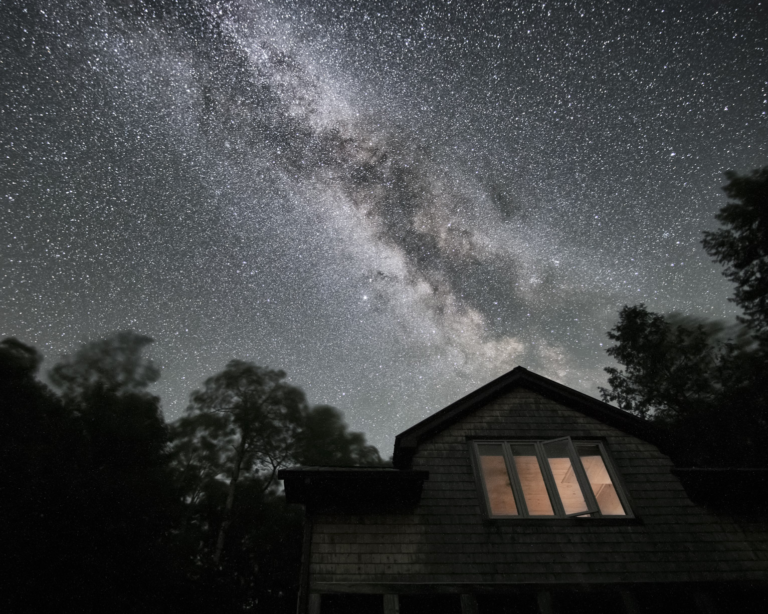 The bright milky way over a cabin and some wind blurred trees